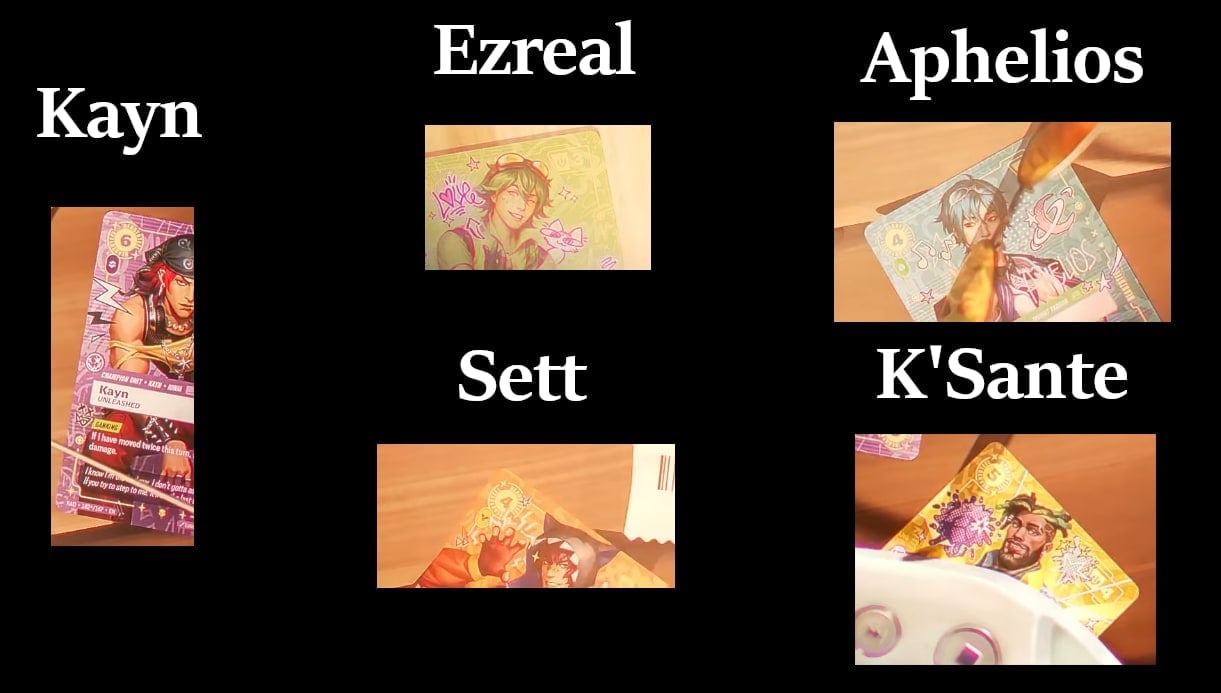 Five Riftbound cards in HEARTSTEEL art from the Live My Life music video, labelled Kayn, Ezreal, Aphelios, Sett and K'Sante, each shown on a wooden table